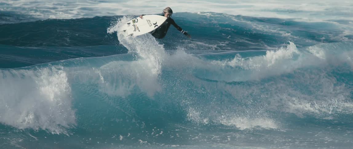 A surfer is riding a big wave as he leaps into the air and spins with his surfboard