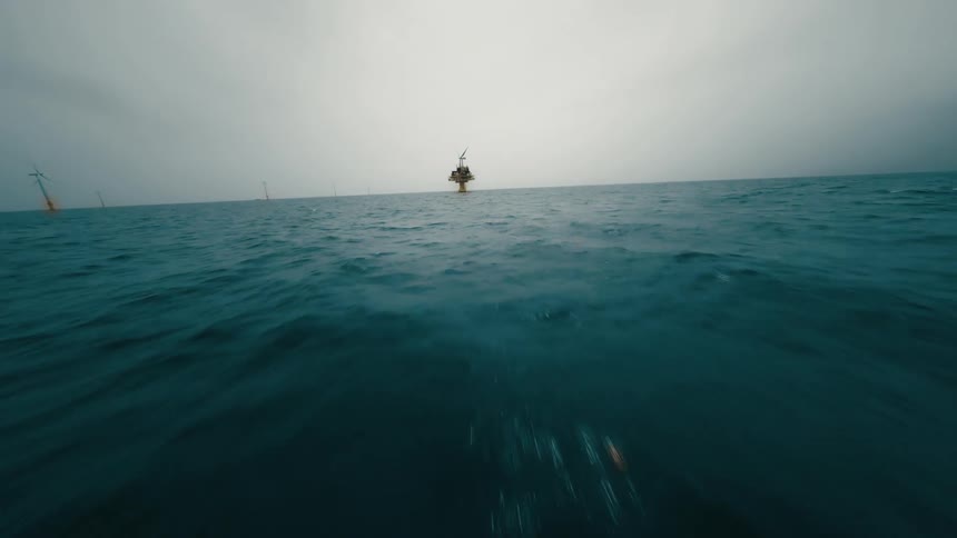 An aerial view over the ocean flying out to a platform
