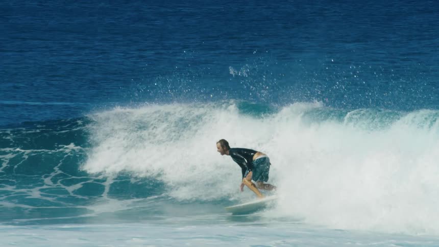 Male surfer with wetsuit and shorts rides ocean wave