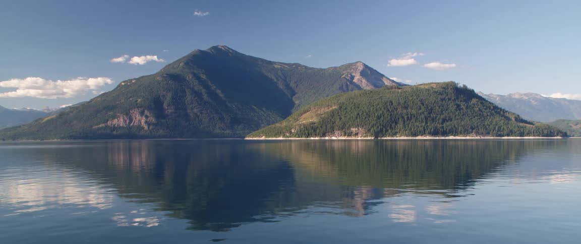Rippling water reflects forest covered mountains under cloudy sky