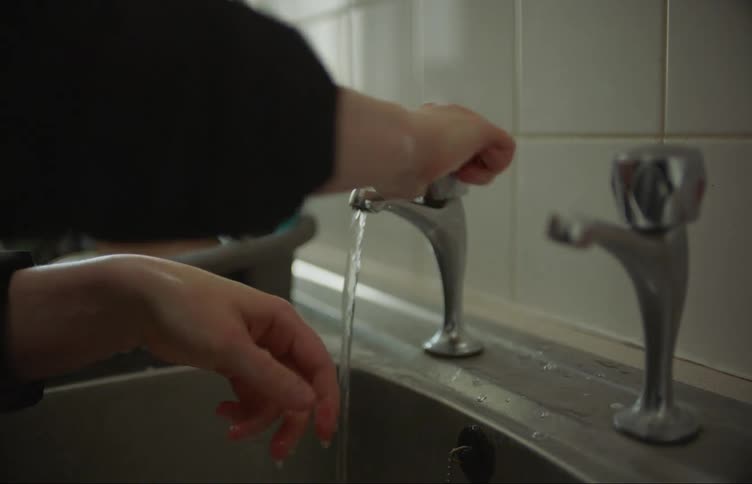 Woman with black sweater washes her hands in kithcen sink in front of white wall tiles