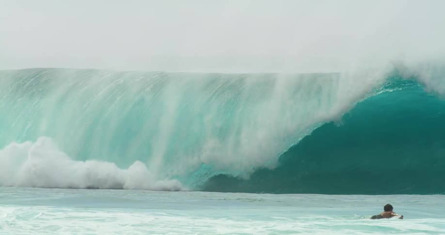 A surfer attempts to stand on their surfboard atop a wave but fails and falls off as the wave crashes on top of them
