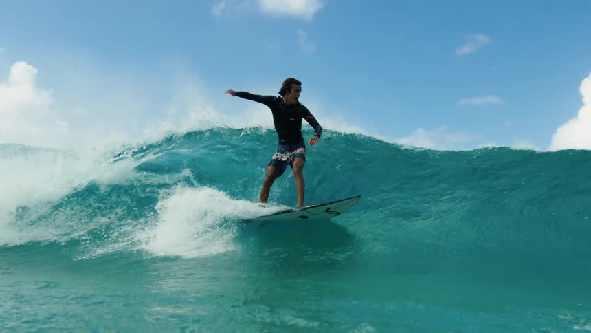 A surfer slowly stands up on his board to ride a wave