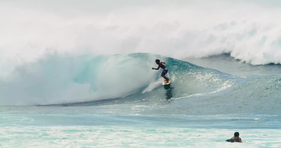A surfer holds his arms out for balance before a large wave knocks him into the water