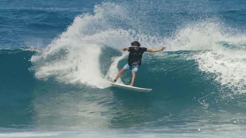 Male surfer rides surfboard up an down crashing wave as other surfers paddle out to sea