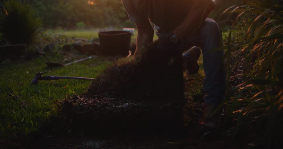 A man uses a hose to spray water on a piece of sod