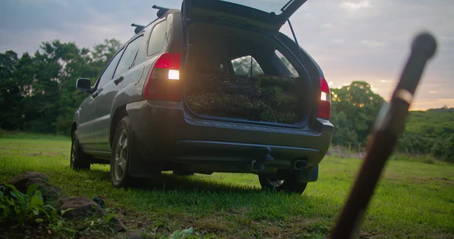 Car with hatchback open loaded with grass backing up to dirt patch