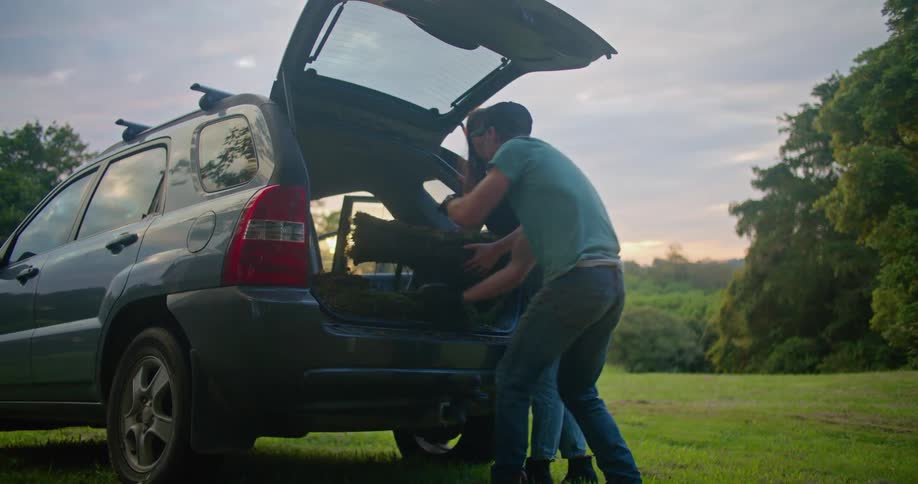 Man and woman unloading some sodding from their car in a grass field at sunset