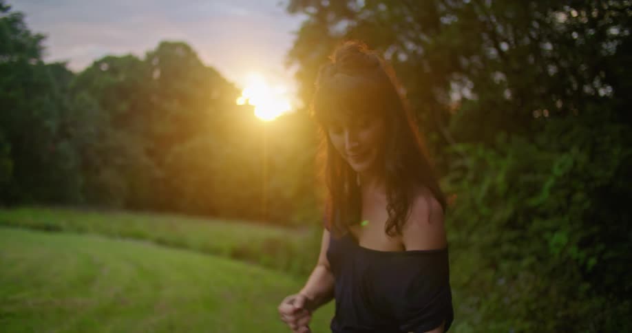 Woman rakes ground near edge of mowed field as sun shine from red sky on the horizon