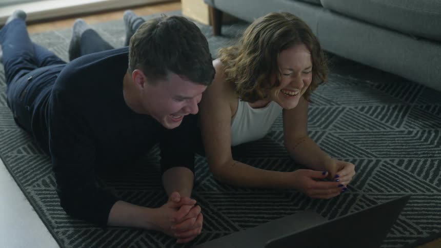 Friends laying on a rug laughing while watching a video on a laptop