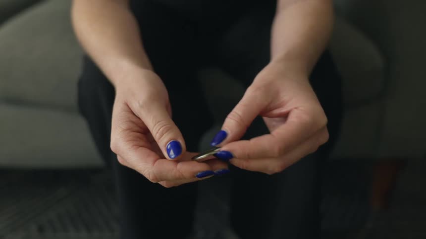 Woman with blue nails holds euro coin sitting on couch in living room at home