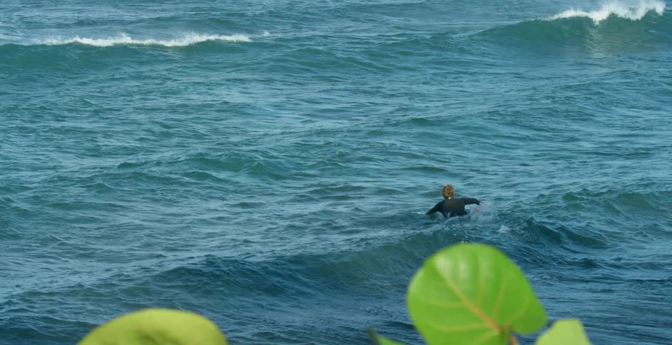 A person paddles their surfboard out in to the ocean