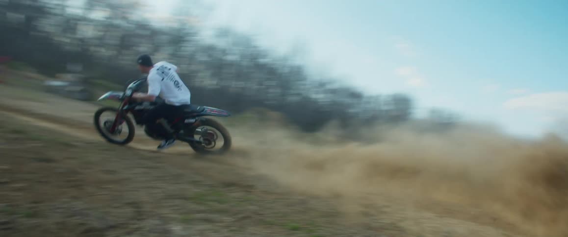 A man takes a steep turn to jump over the hill on his dirt bike