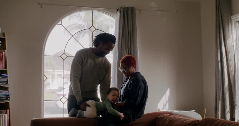 Young black family playing with the baby near a large picture window