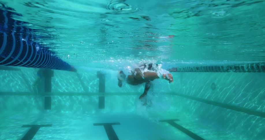 Man wears goggles and a swim cap as he swims along pool lane