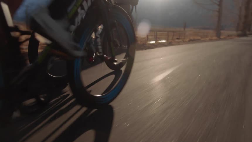 Cyclists race each other riding down highway past fenced pasture bordered by mountains