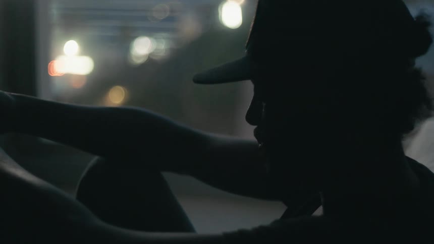 Silhouette of a young man weaing a baseball cap sitting inside a dimly lit room at night