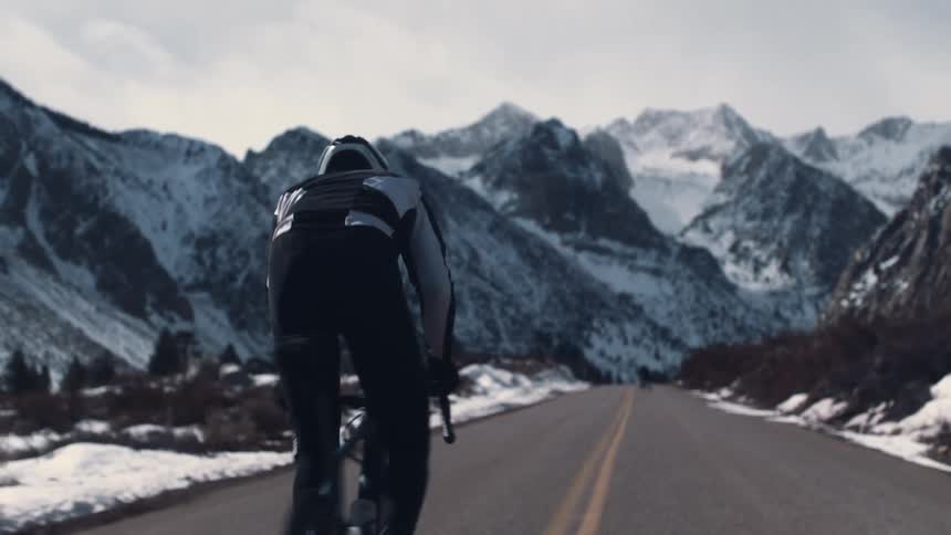 Man riding a bicycle on a road on a road near the snow covered mountains at sunset