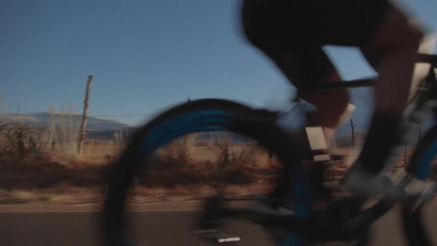 Cyclist rides bicycle along highway past pasture as sun shines over mountains