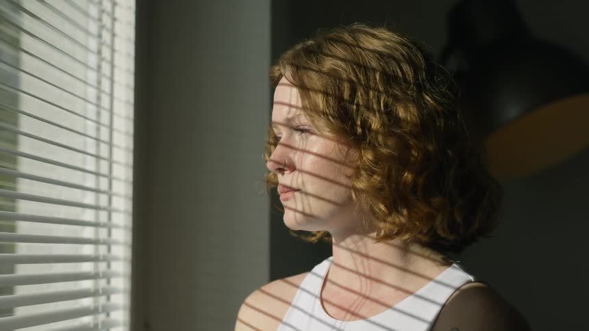 Young blonde woman looking out the window at home in the morning