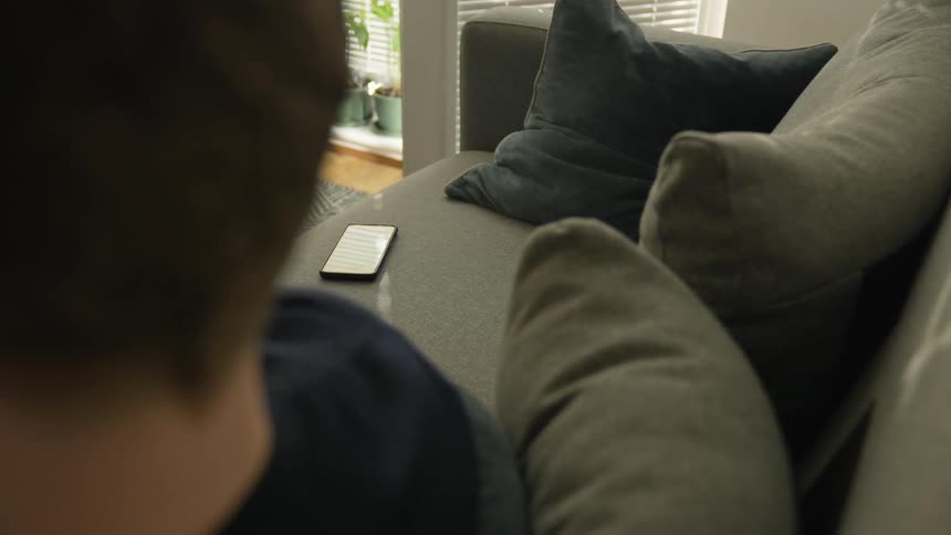 Smartphone resting on the couch next to a man in the living room at home