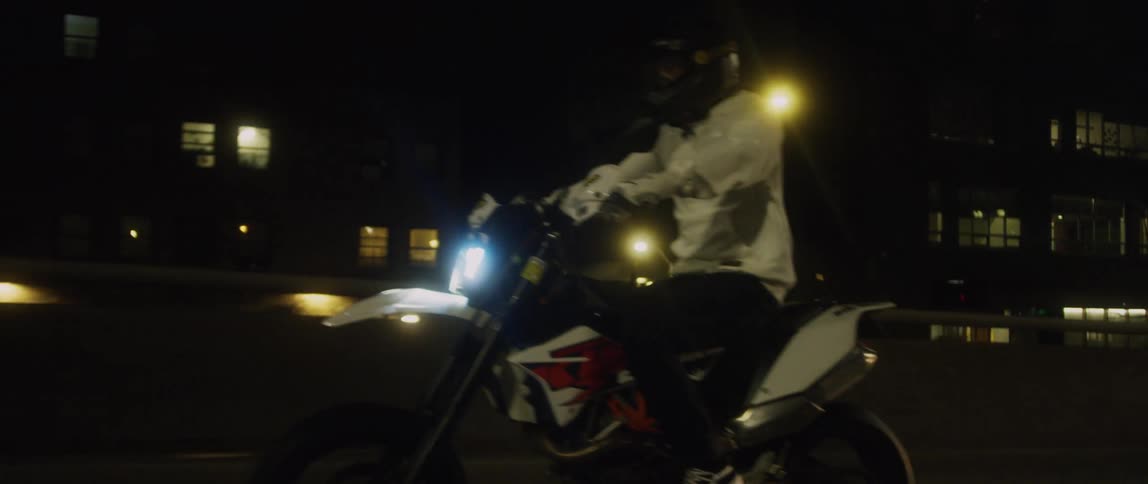 Man on a dirt bike speeding down the road near city buildings at night
