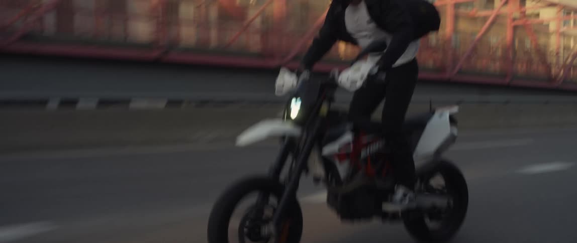 A man driving a motorcycle down a city street stands up and does a wheelie