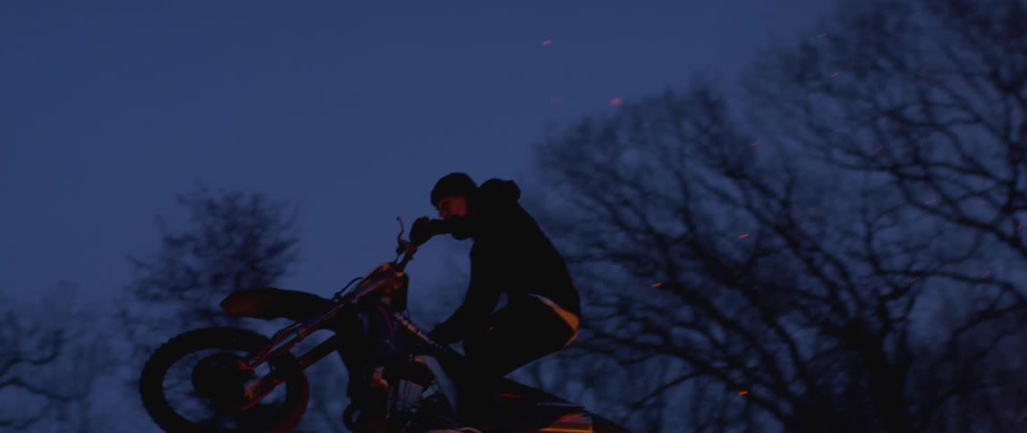A man rides a dirt bike using a ramp to jump over a bonfire