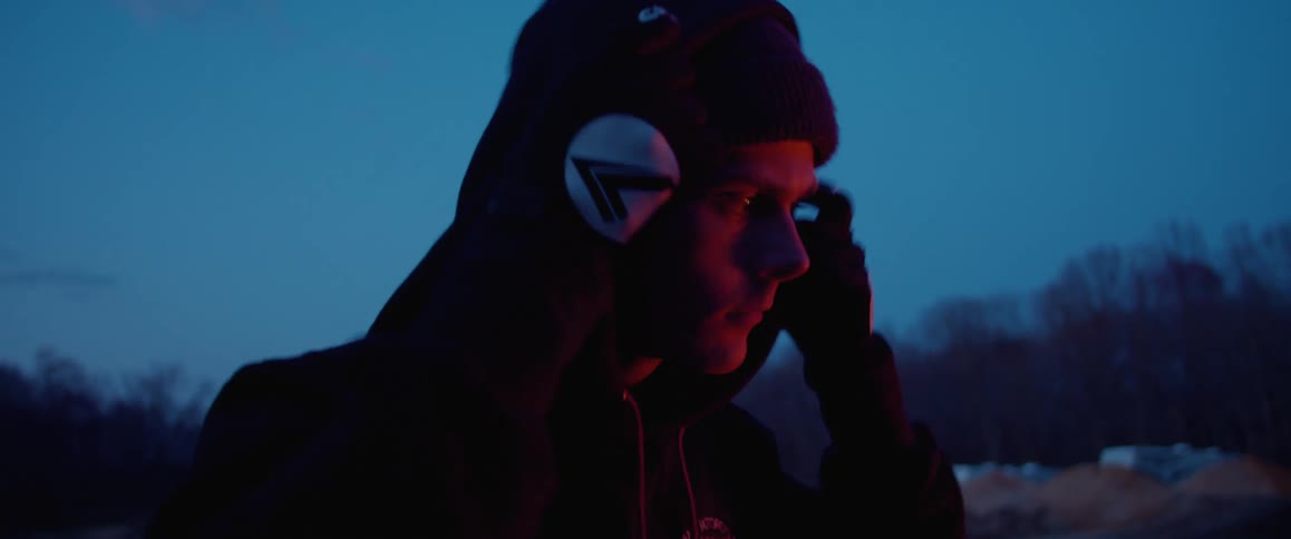 A man adjusts the hood on his head while standing outdoors at night