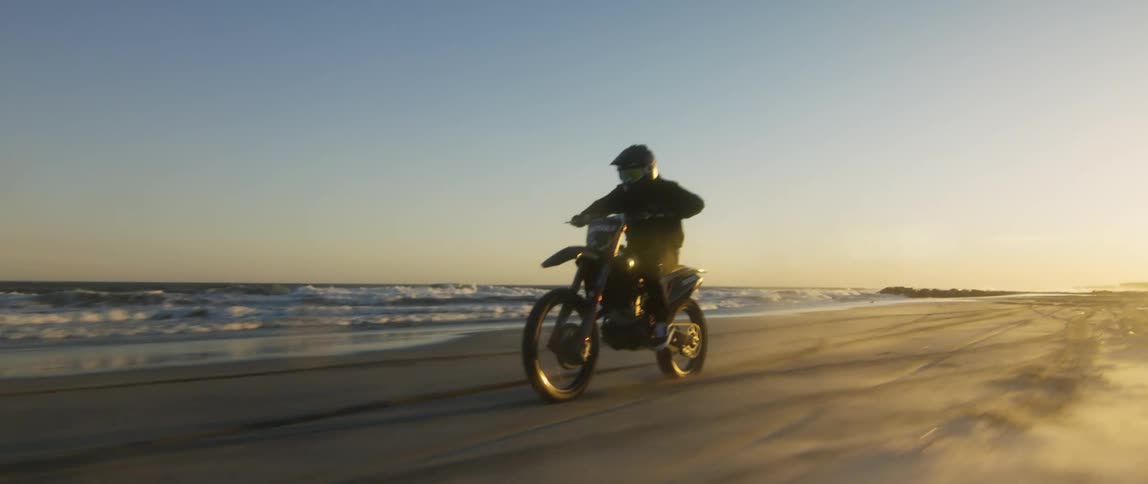 A man is riding a motorcycle on a beach and popping wheelies