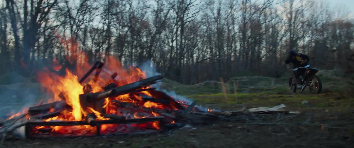 A cyclist rides his motorcycle near a bonfire in the woods