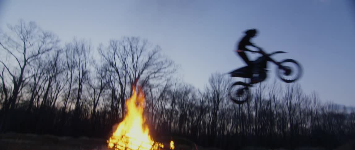 A motorcycle rider leaps over a bonfire
