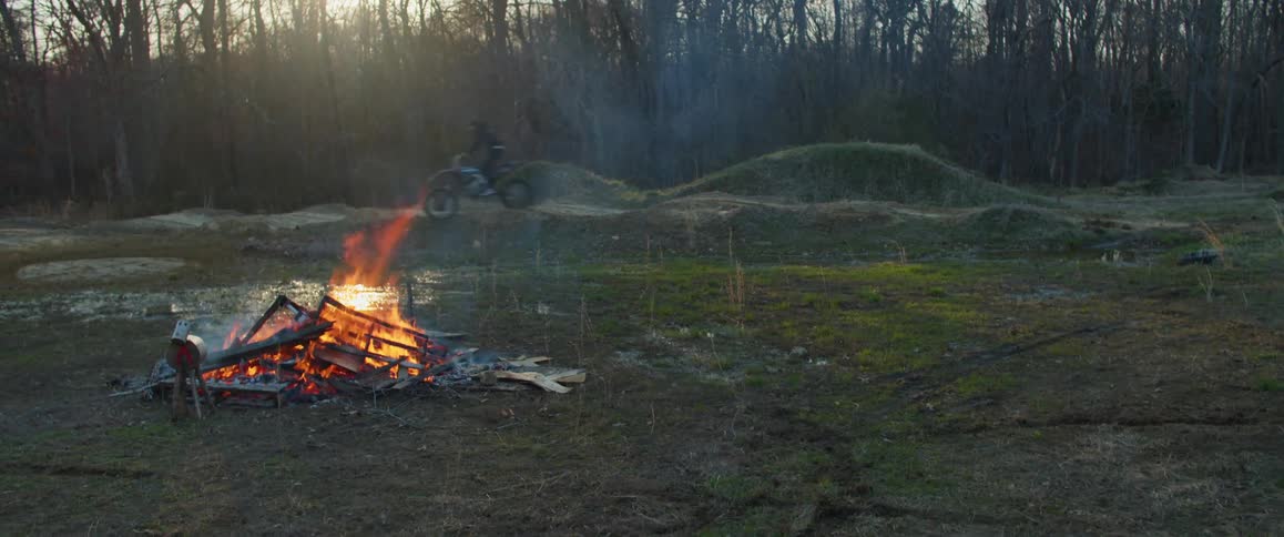 A man is riding a dirt bike in circles next to a bonfire