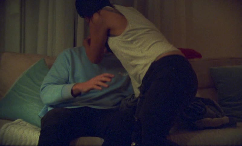 Man with blue sweater black pants and woman wearing white shirt and black pants make out with each other on sofa in living room at home