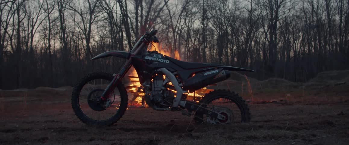 A motorcycle is parked in front of a bonfire near the woods