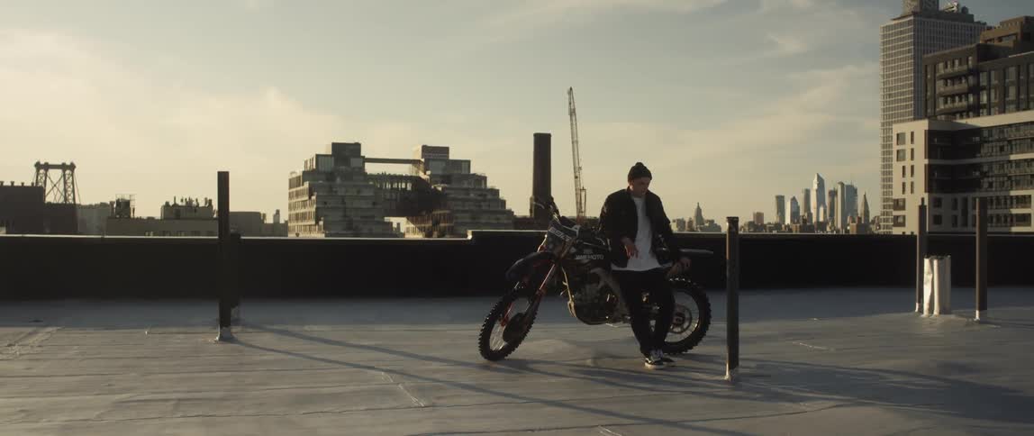 Man sitting on a motorcycle over the roof of a building in front of the city skyline at sunset