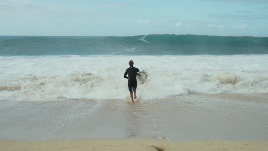 Surfer running into the ocean towards a large wave