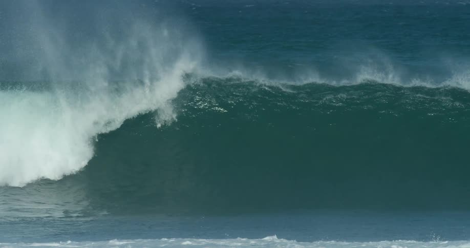 A surfer paddling out rides over the crest of a wave before it curls and breaks