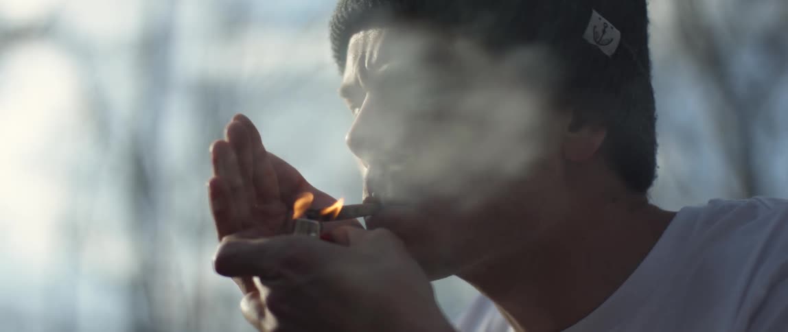 Man sits on motorcycle smoking with leafless woods in the background