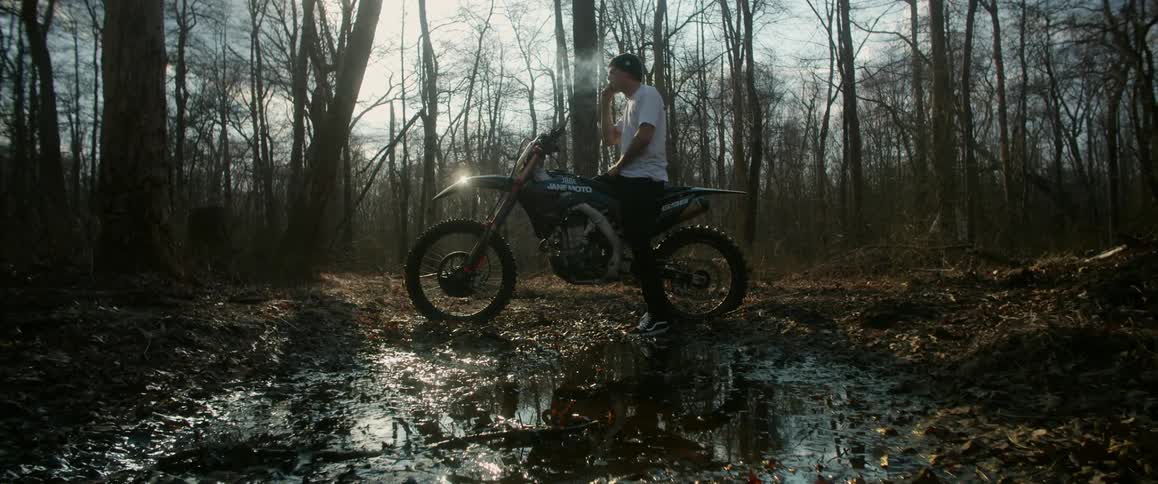 Man smokes while sitting on motorcycle parked in puddle in forest