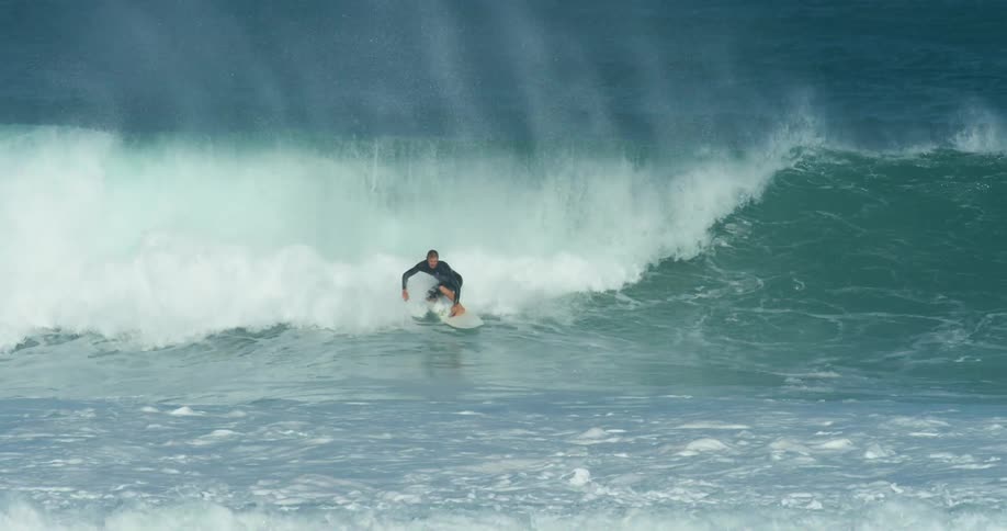 Male surfer with wetsuit rides big wave on surfboard