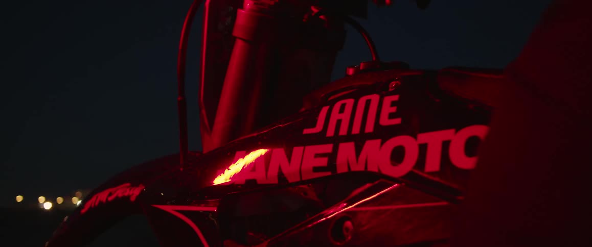 Rider sits on motorcycle labeled with a brand name at night