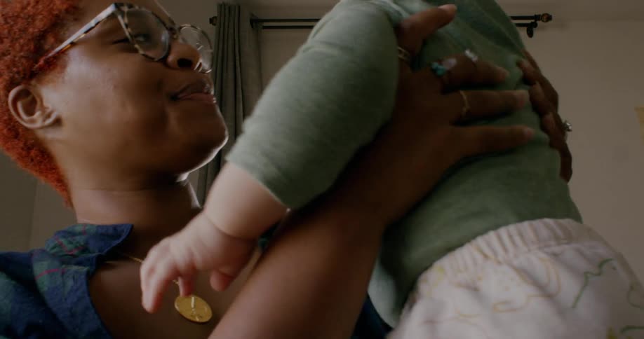 A woman smiles while lifting an infant indoors during the day