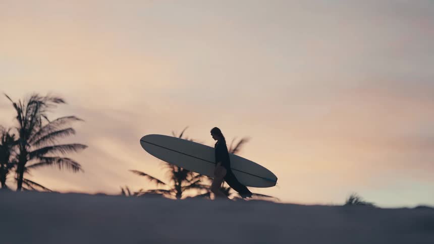 A woman is walking with a surfboard on the coast of a beach