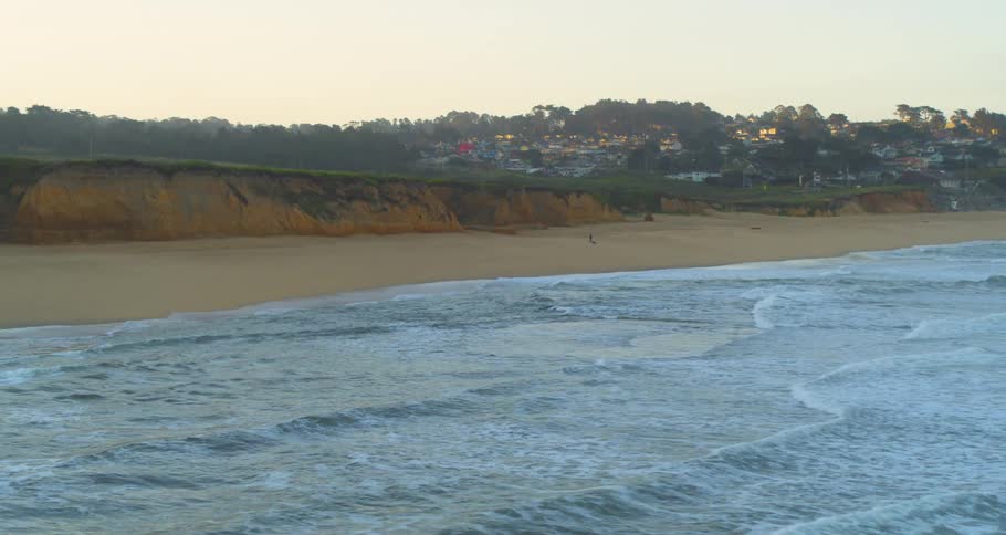 Ocean waves wash into a beach outside of a small town in the evening