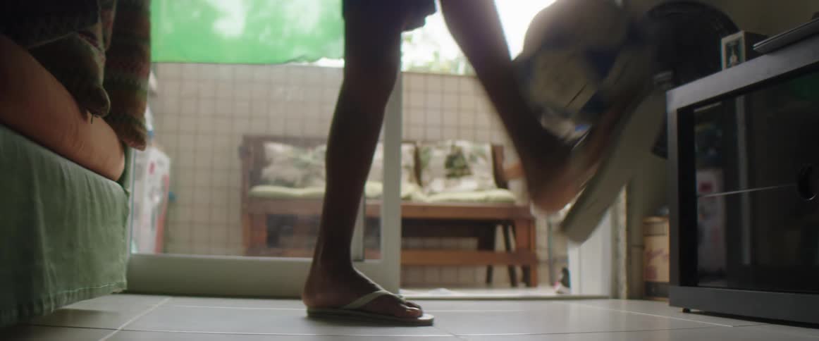 Person wearing shorts plays with soccer ball while standing in living room with open sliding glass doors in background