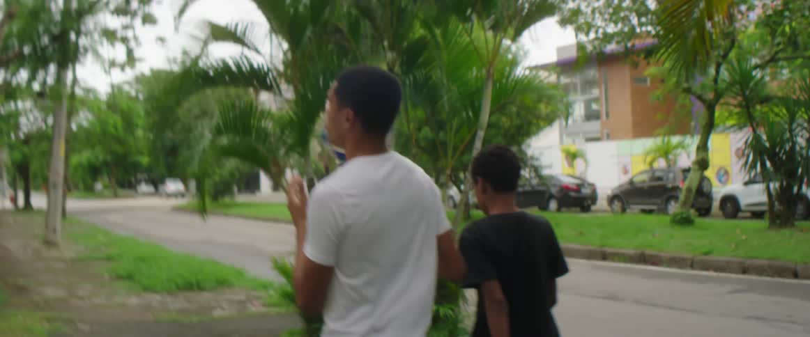 A pair of young men walk together leisurely through a neighborhood while carrying a soccer ball