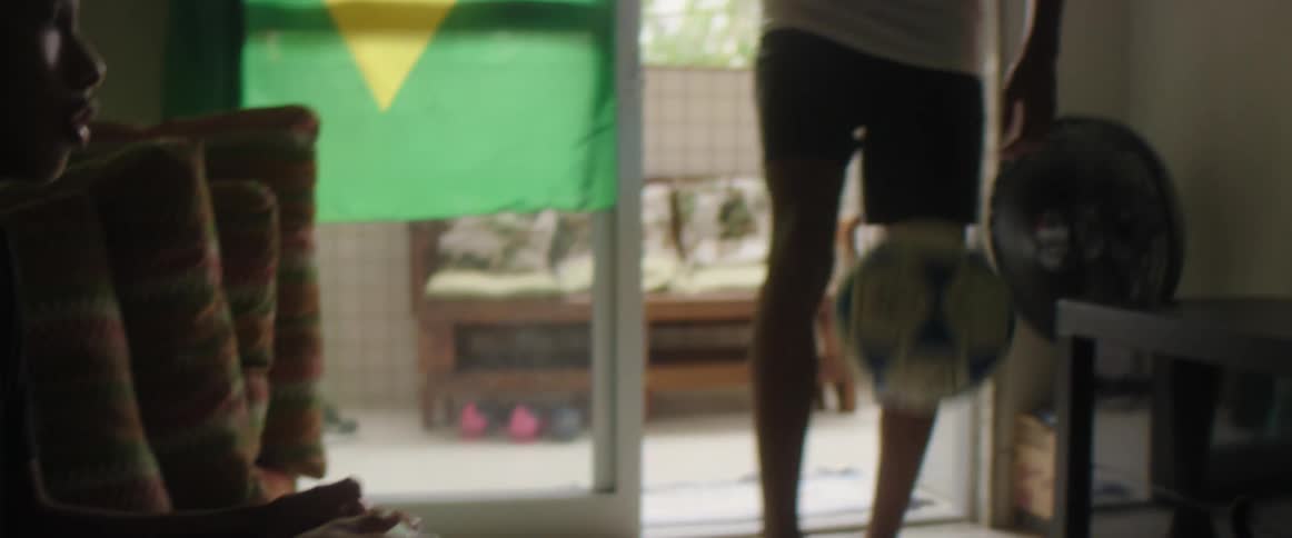 Boy sitting on the couch plays video while another plays with a football at home