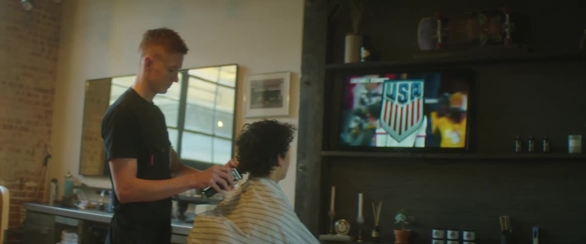 A teenager watches a soccer match in a barber while getting his hair cut