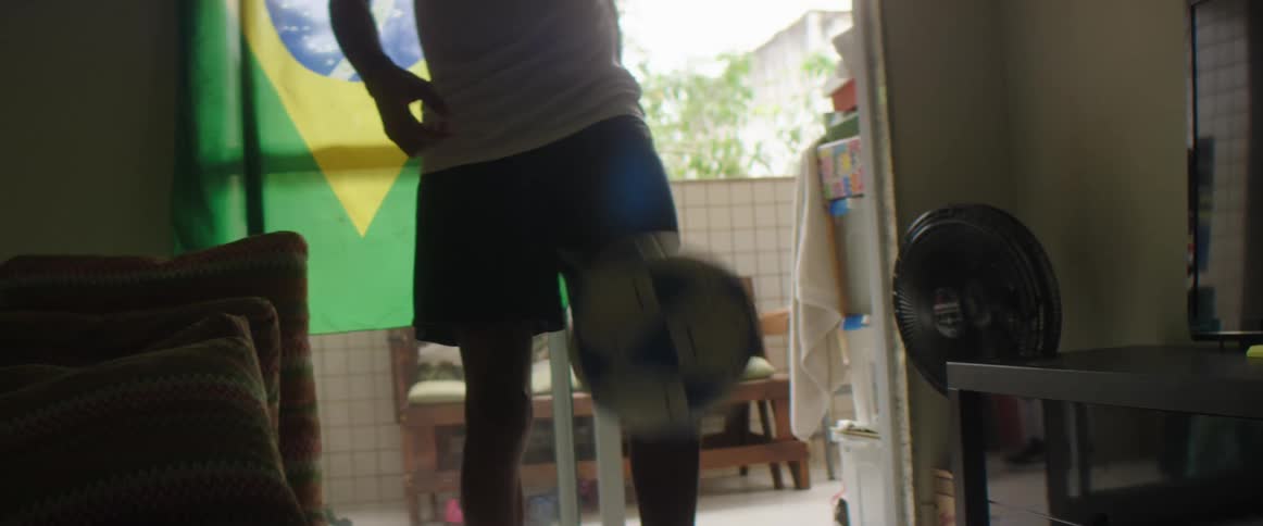 Man practices with soccer ball in living room with open sliding glass doors